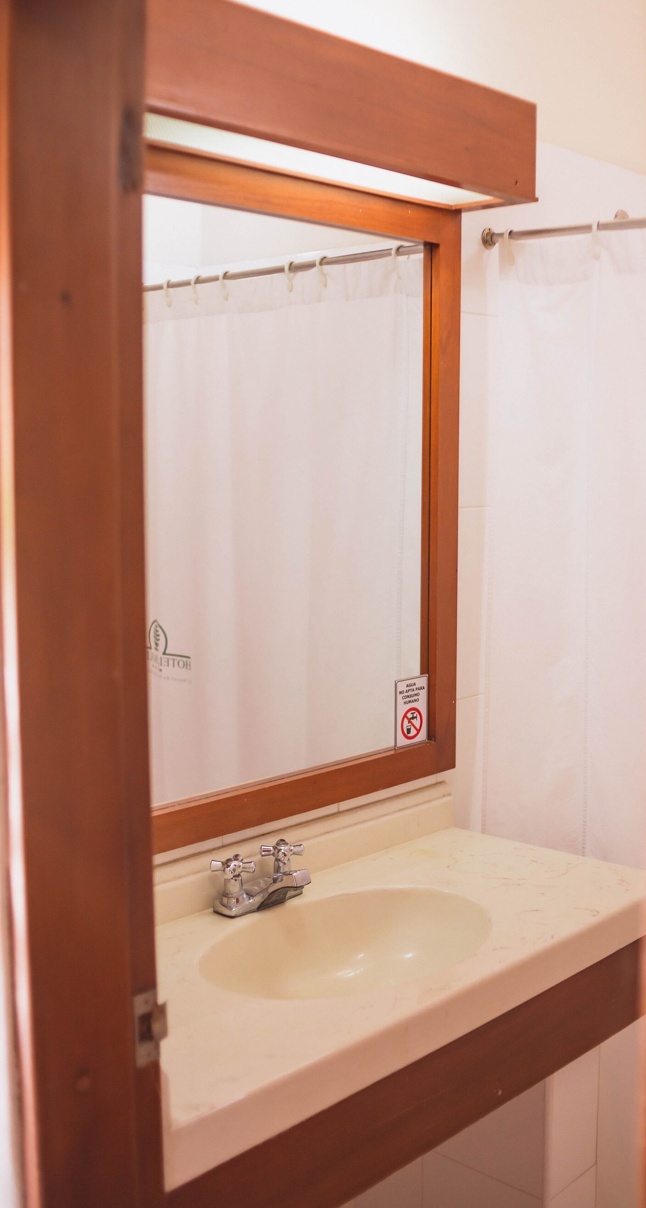 Un baño con un espejo de marco de madera, un lavamanos y una cortina de ducha.