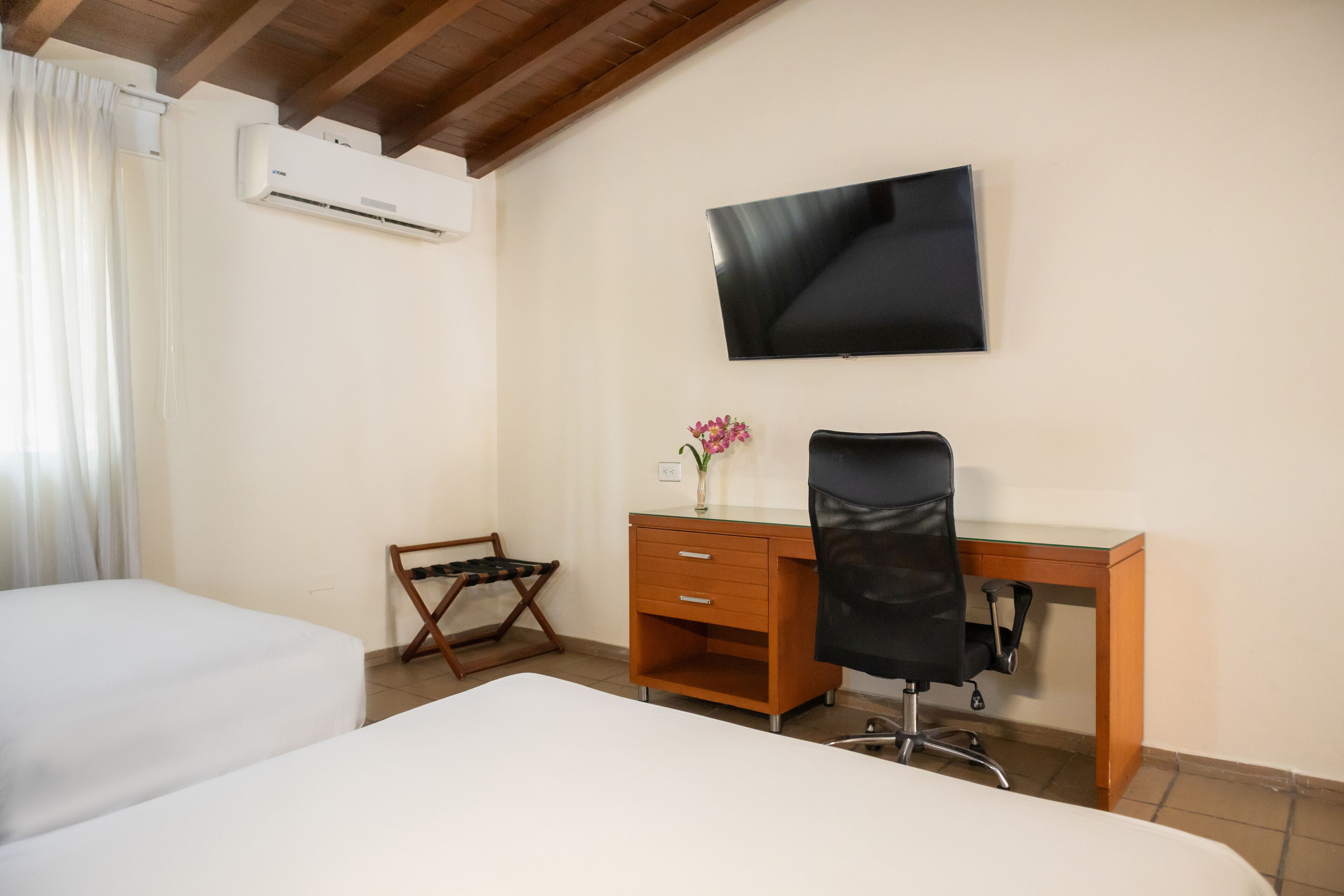 Een hotelkamer met twee bedden, een bureau met een stoel, een televisie en een airconditioner.