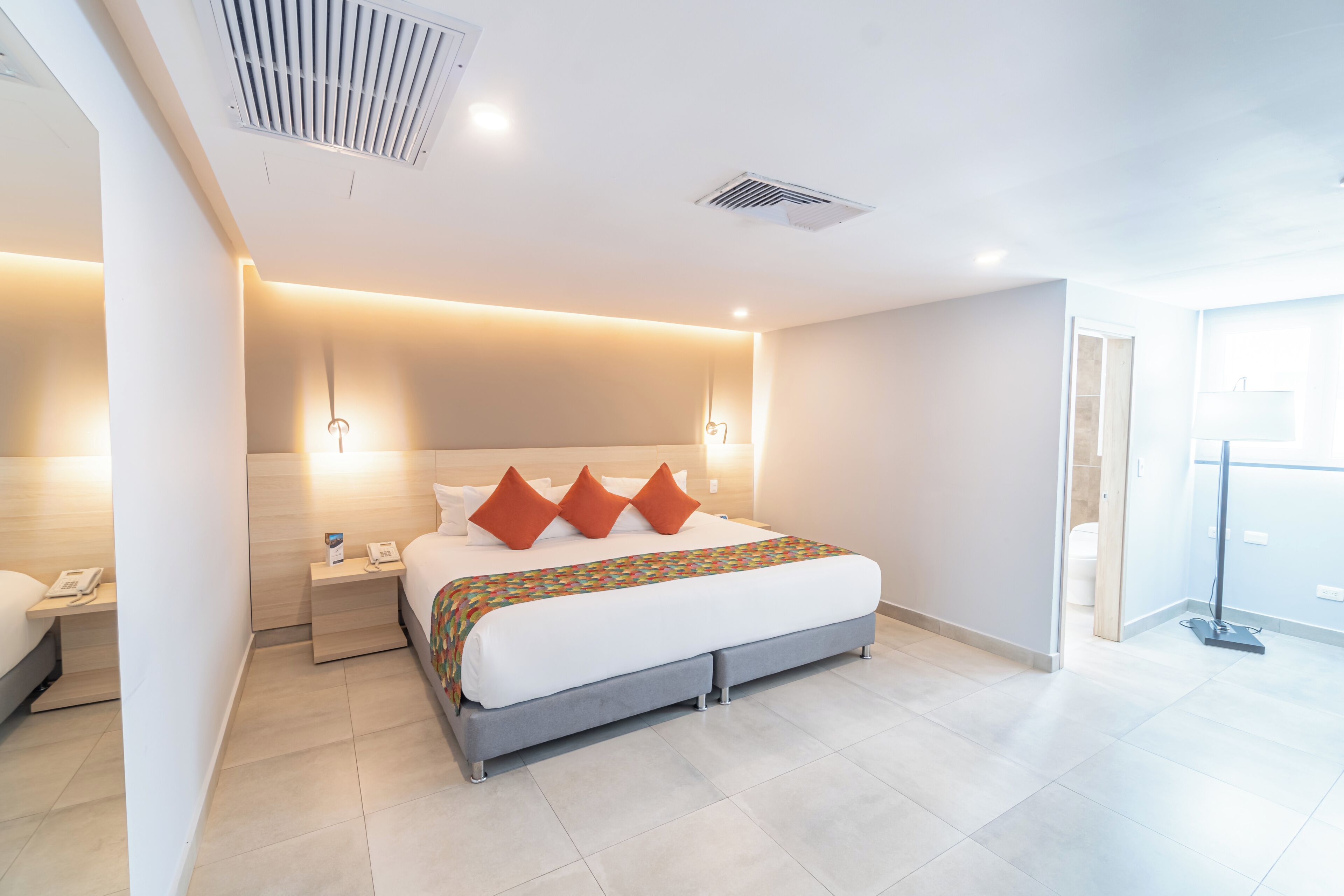 A modern hotel room with a large bed, bedside tables, a phone, and a visible bathroom.