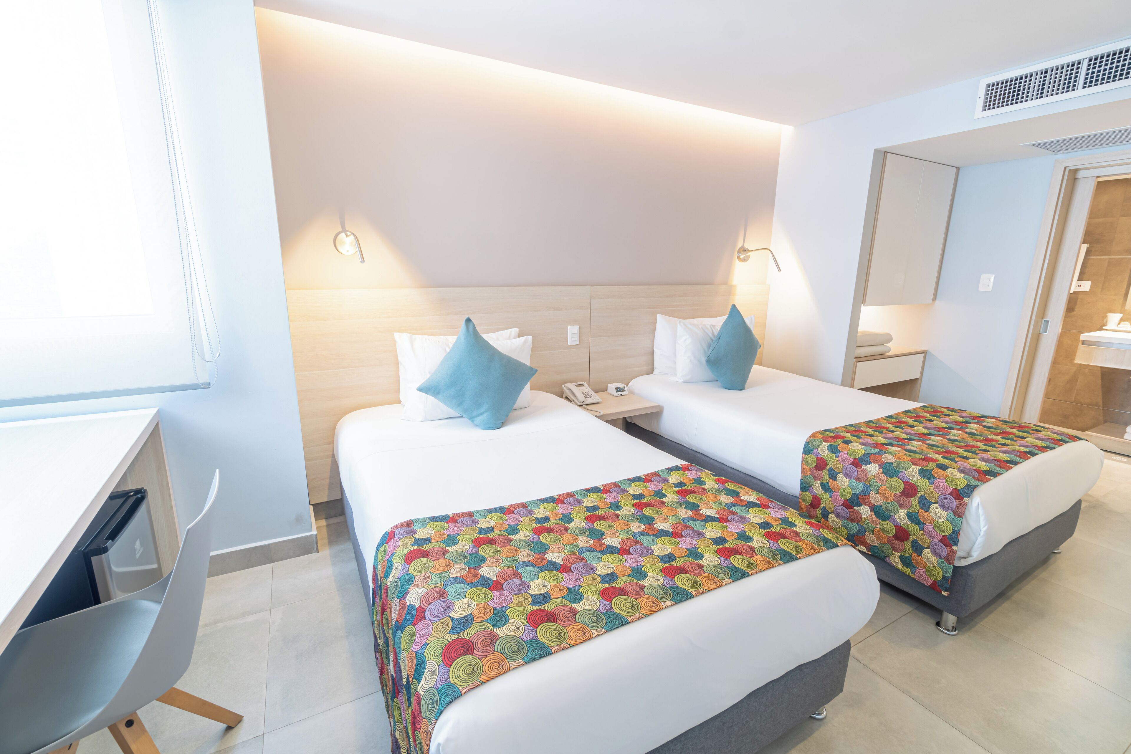 A hotel room with two beds, a desk, and a mirror.