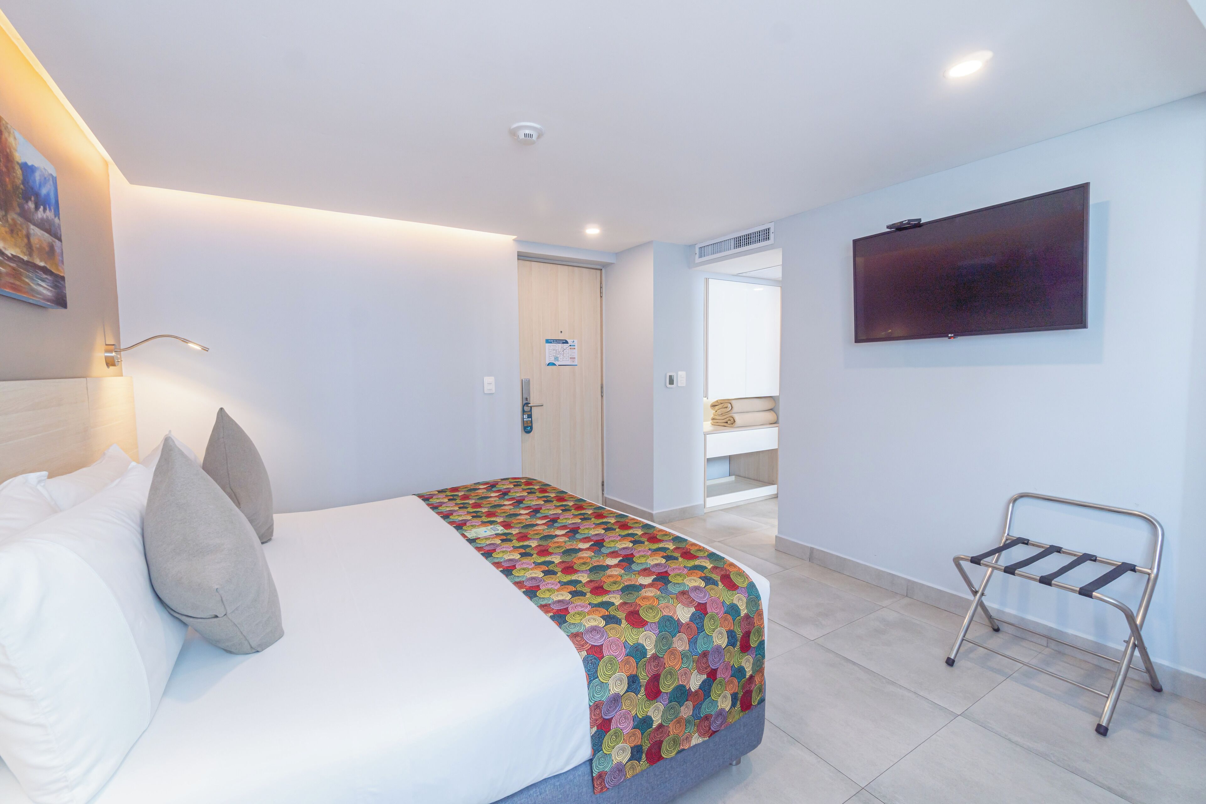 A hotel room with a bed, a TV mounted on the wall, and a small seating area with a metal frame.