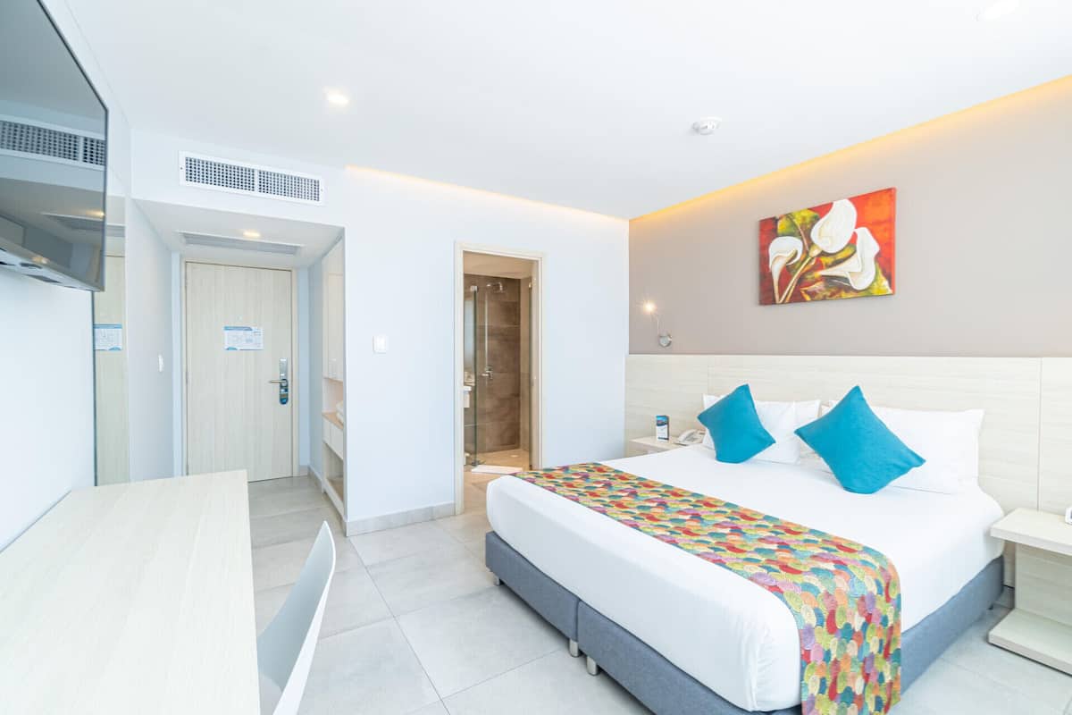 Una habitación de hotel con cama, mesita de noche y zona de ducha.
