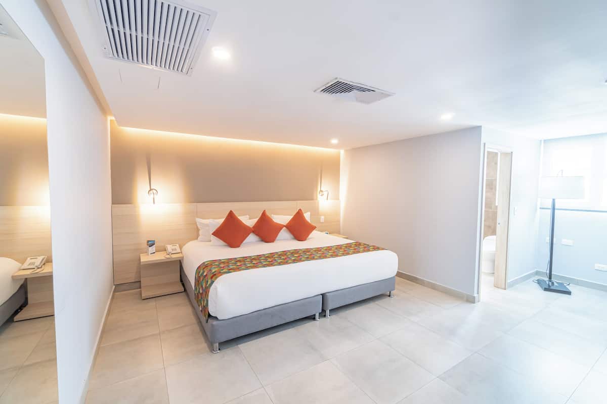 Una habitación de hotel moderna con una cama grande, mesitas de noche, un teléfono y una puerta de baño visible.