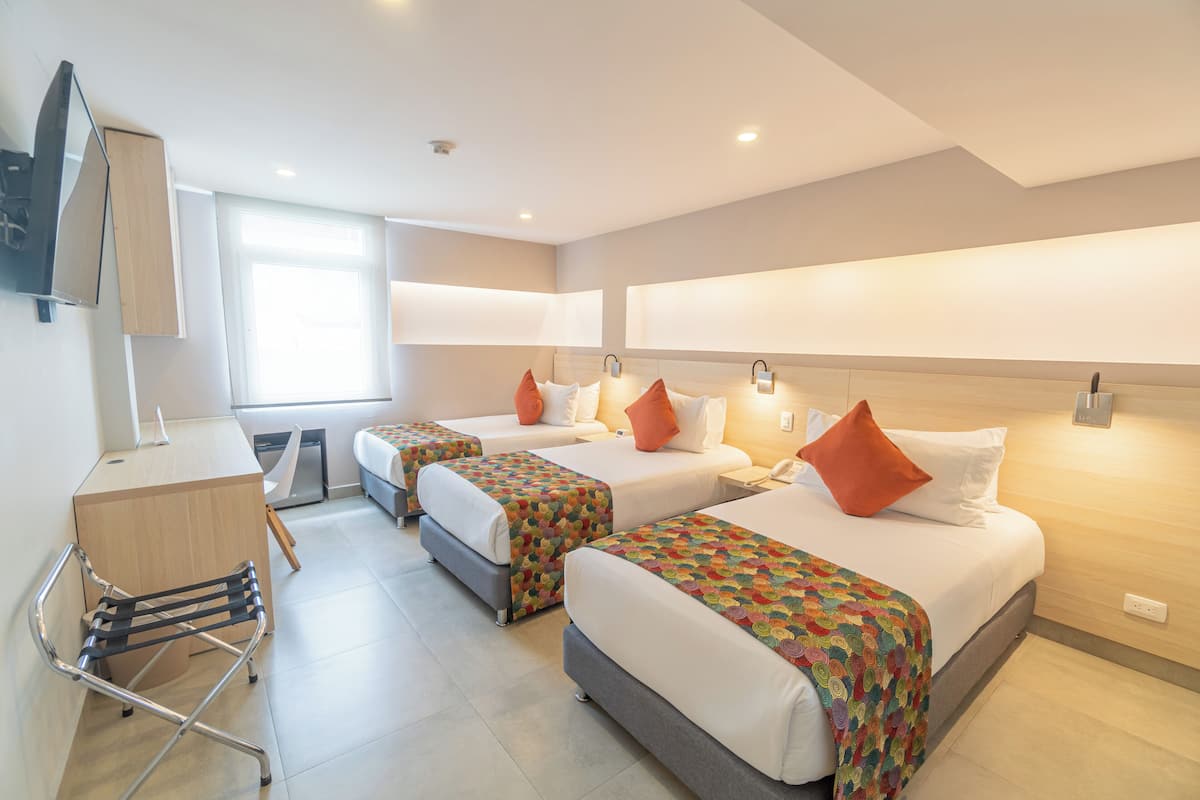 Habitación de hotel con tres camas, un escritorio y televisión.