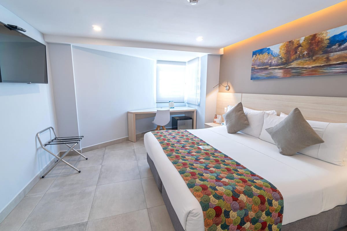 Habitación de hotel con cama, escritorio, silla, televisor y un cuadro en la pared.