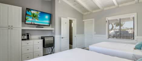 A bedroom with two beds, a TV on the wall, a coffee maker, and a door leading to another room.