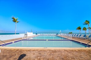 A swimming pool with a 2 FT depth marker, surrounded by lounge chairs and palm trees, with a view of the ocean.