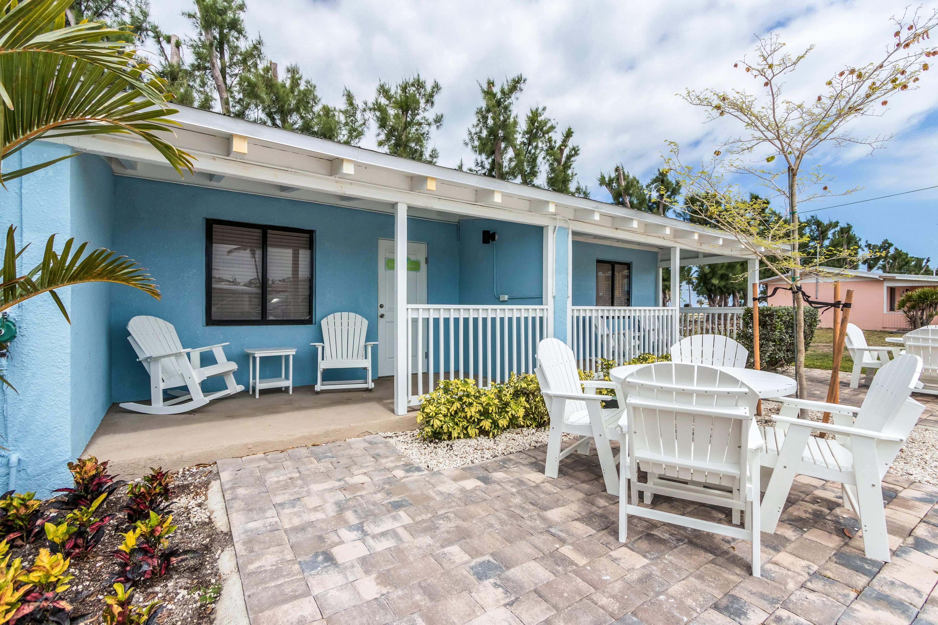 A blue building with a covered patio area featuring white Adirondack chairs and a small table.