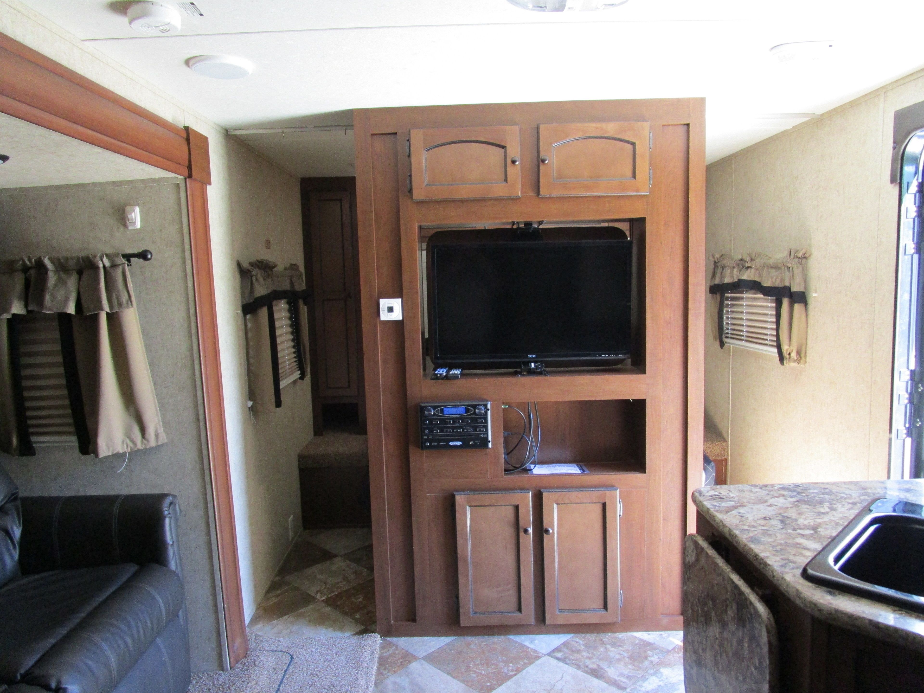 A compact RV interior with a kitchenette, a seating area, and a television mounted on a cabinet.