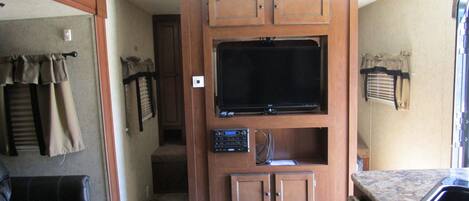 A compact RV interior with a kitchenette, a seating area, and a television mounted on a cabinet.