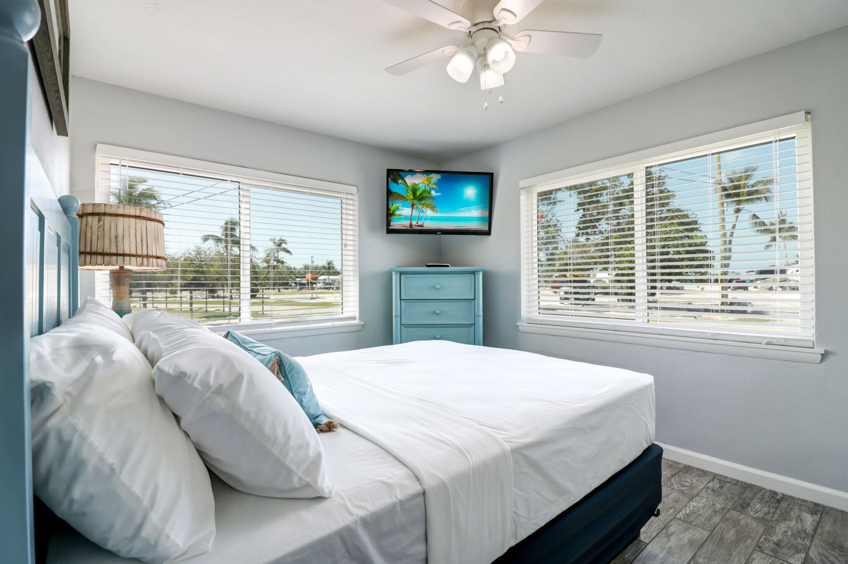 A bedroom with a bed, a TV, and two windows with blinds.