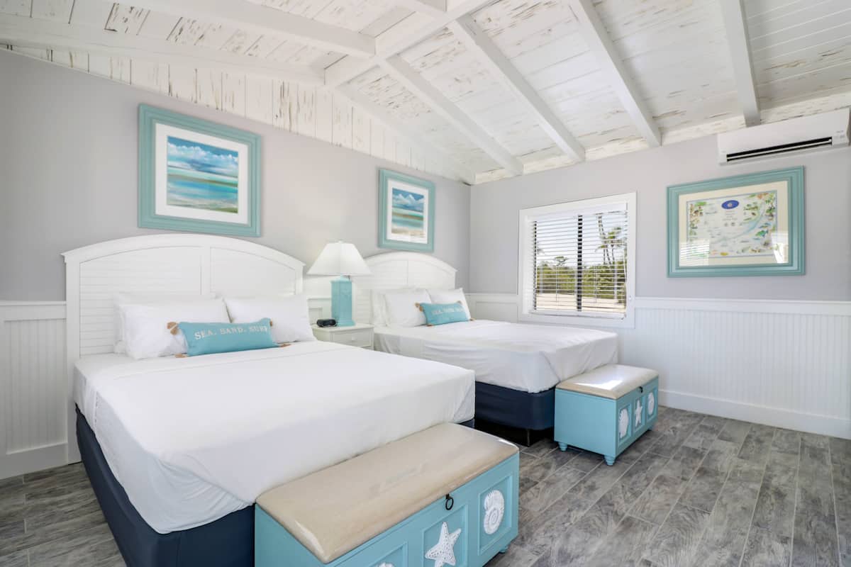 A bedroom with two beds, a window with blinds, and a ceiling with exposed beams.