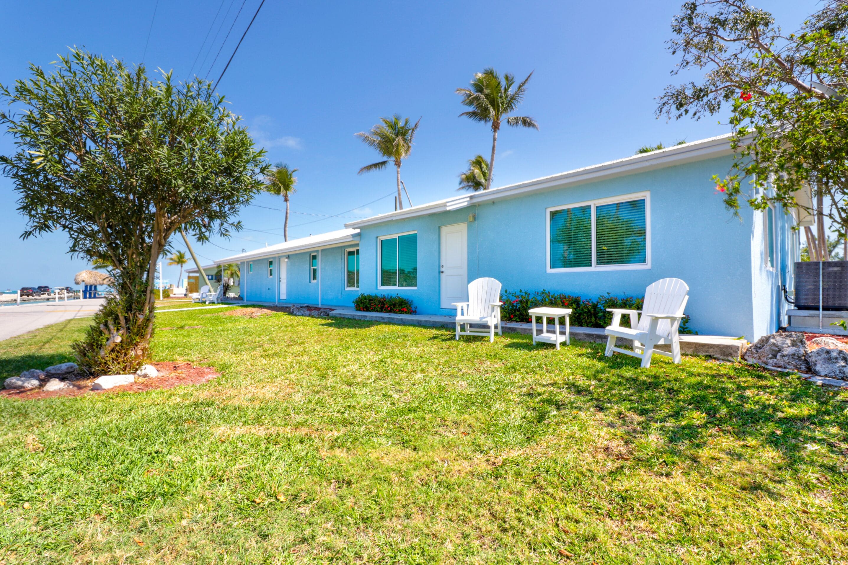 A row of blue motel buildings with white exterior walls, a grassy lawn, and a few trees.