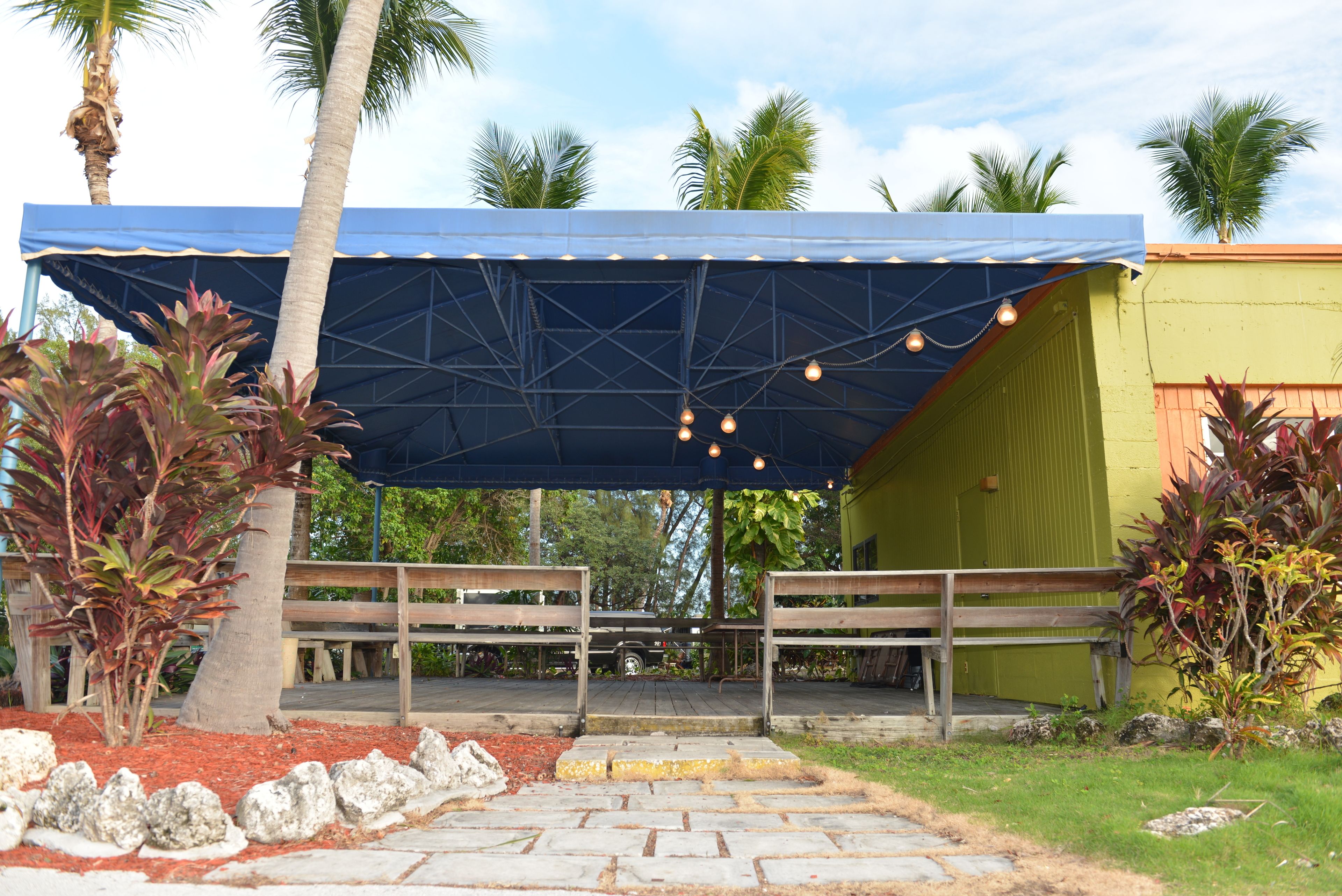 An outdoor covered area with a blue roof, wooden benches, and string lights.