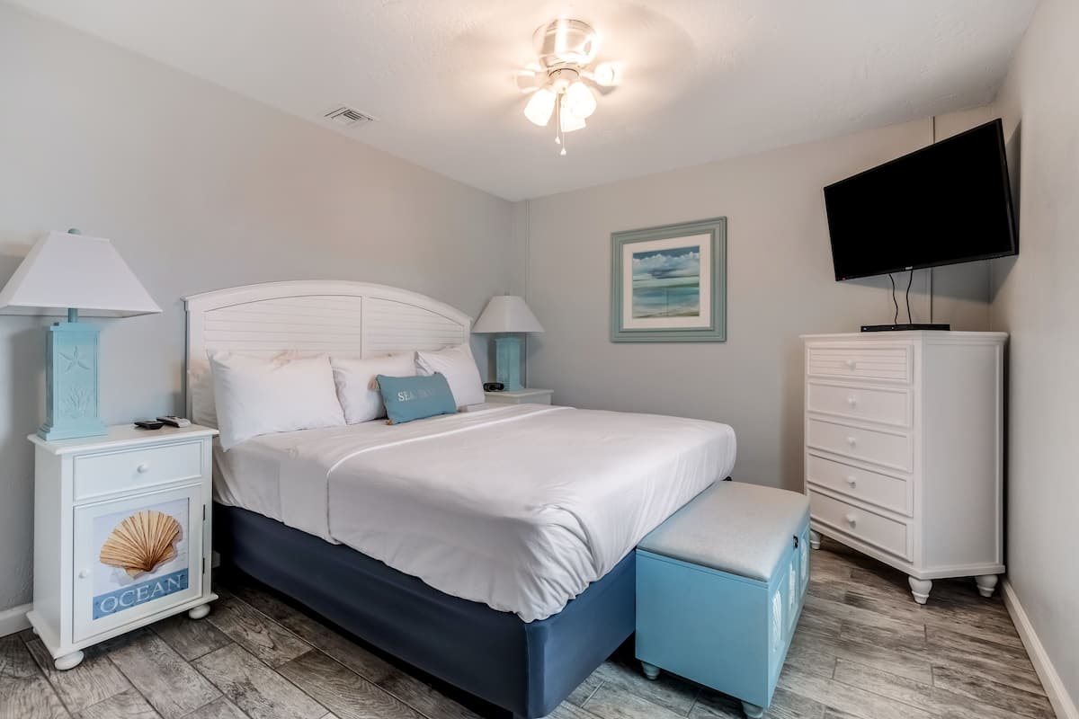 A bedroom with a bed, nightstands, a dresser, a television, and a ceiling fan.