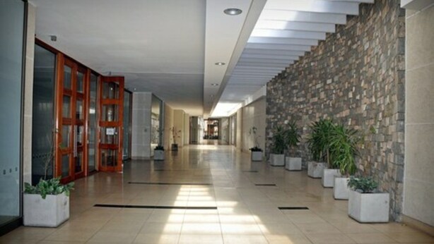 Een moderne hotel lobby met een lange gang, houten deuren, een stenen muur en potplanten.
