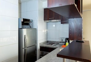 Una cocina compacta con un refrigerador de acero inoxidable, un microondas y una estufa a gas.