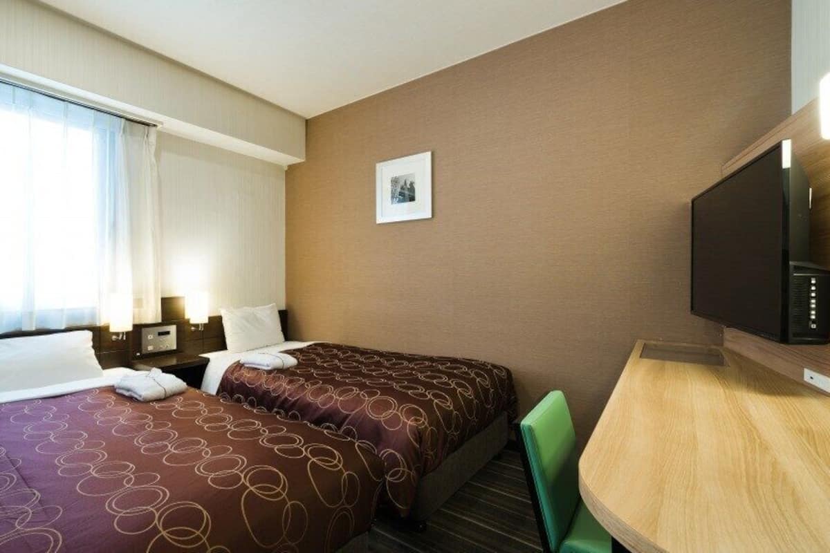 A hotel room with two beds, a desk, a television, and a picture on the wall.