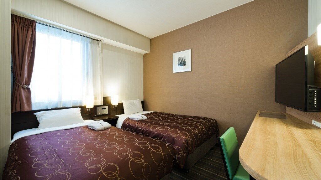 A hotel room with two beds, a desk, a television, and a window with curtains.