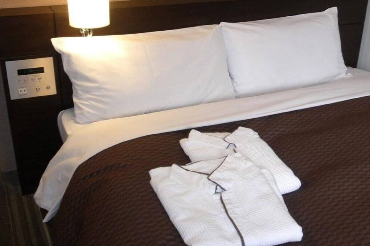 A neatly made bed with white linens, a brown blanket, and a folded white garment on the bed.
