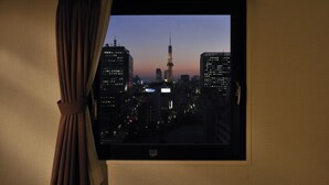 Vista desde una ventana de un paisaje urbano al atardecer, con edificios iluminados y una torre destacada.