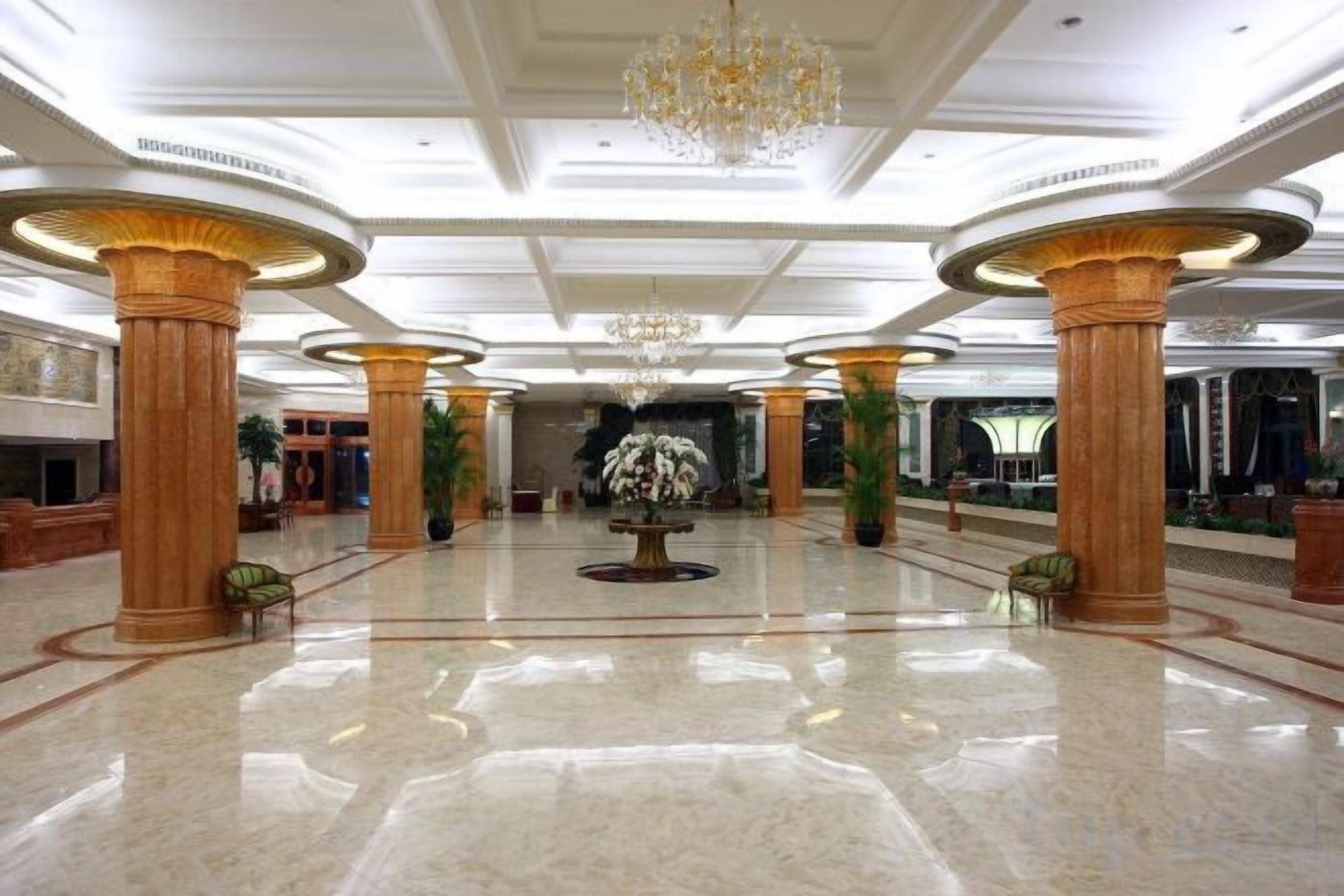 Un hall espacioso con suelo de mármol, amplias columnas y un arreglo floral central.
