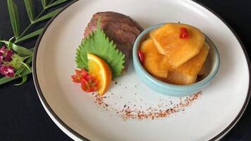 A plate with a bowl of food, a piece of meat, and some garnishes.
