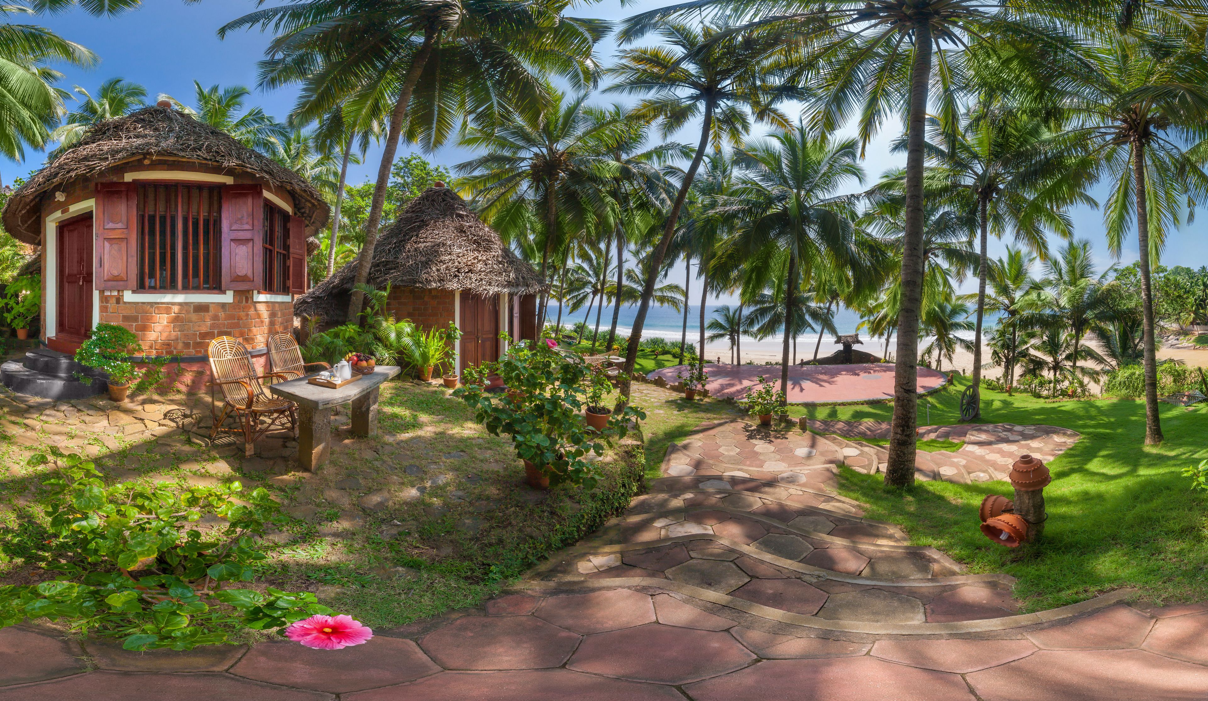 Un complexe hôtelier tropical doté de bungalows aux toits de chaume, d’un sentier en pierre et de palmiers.