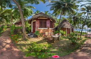 Un bungalow au toit de chaume, doté d’un petit patio et entouré d’une végétation luxuriante et de palmiers.
