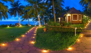 A tropical resort with a thatched-roof building, a paved pathway lined with lights, and palm trees. - Soma Manaltheeram Ayurveda Beach Village (Neyyattinkara)