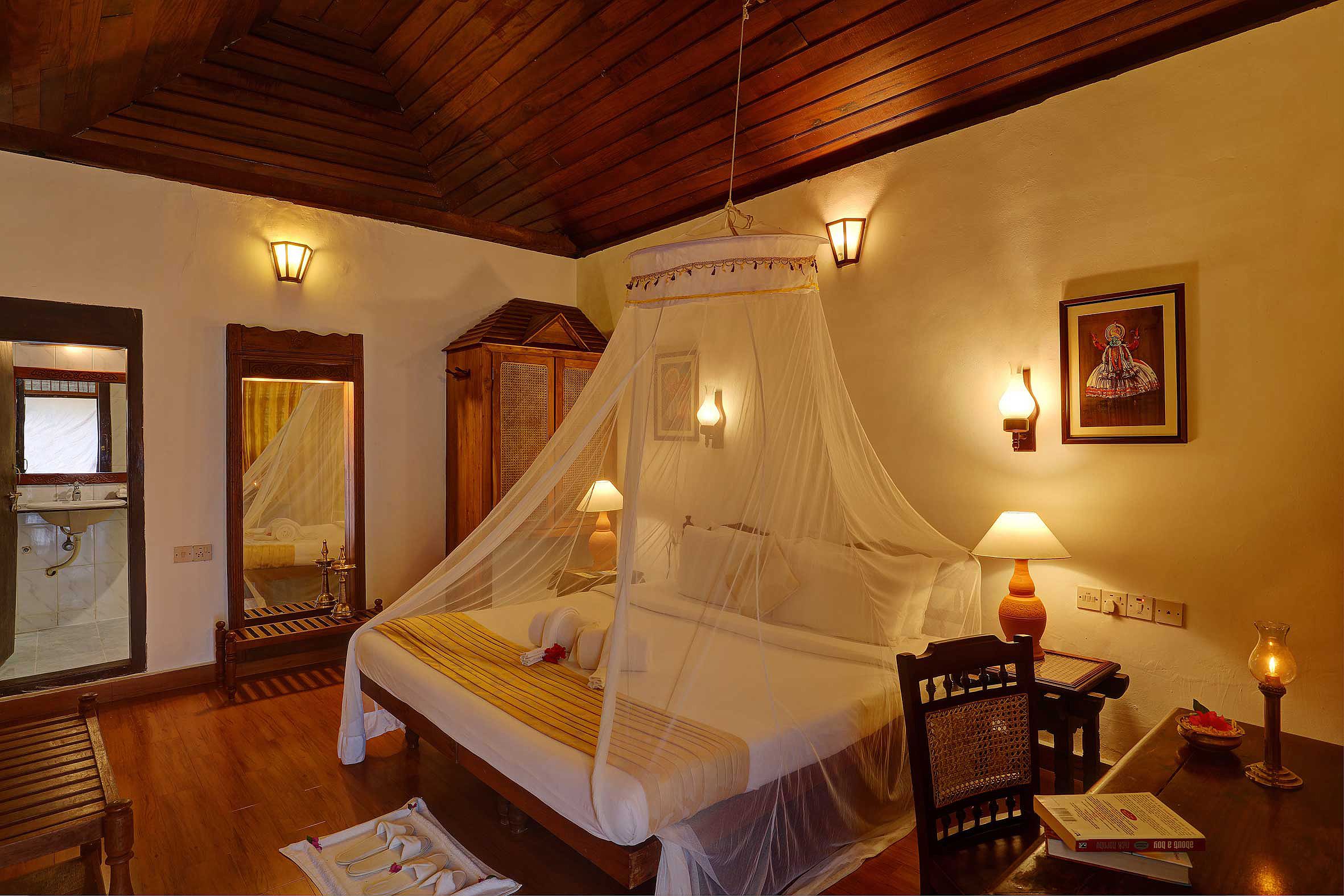 A bedroom with a four-poster bed, a wooden ceiling, and wall-mounted lamps.