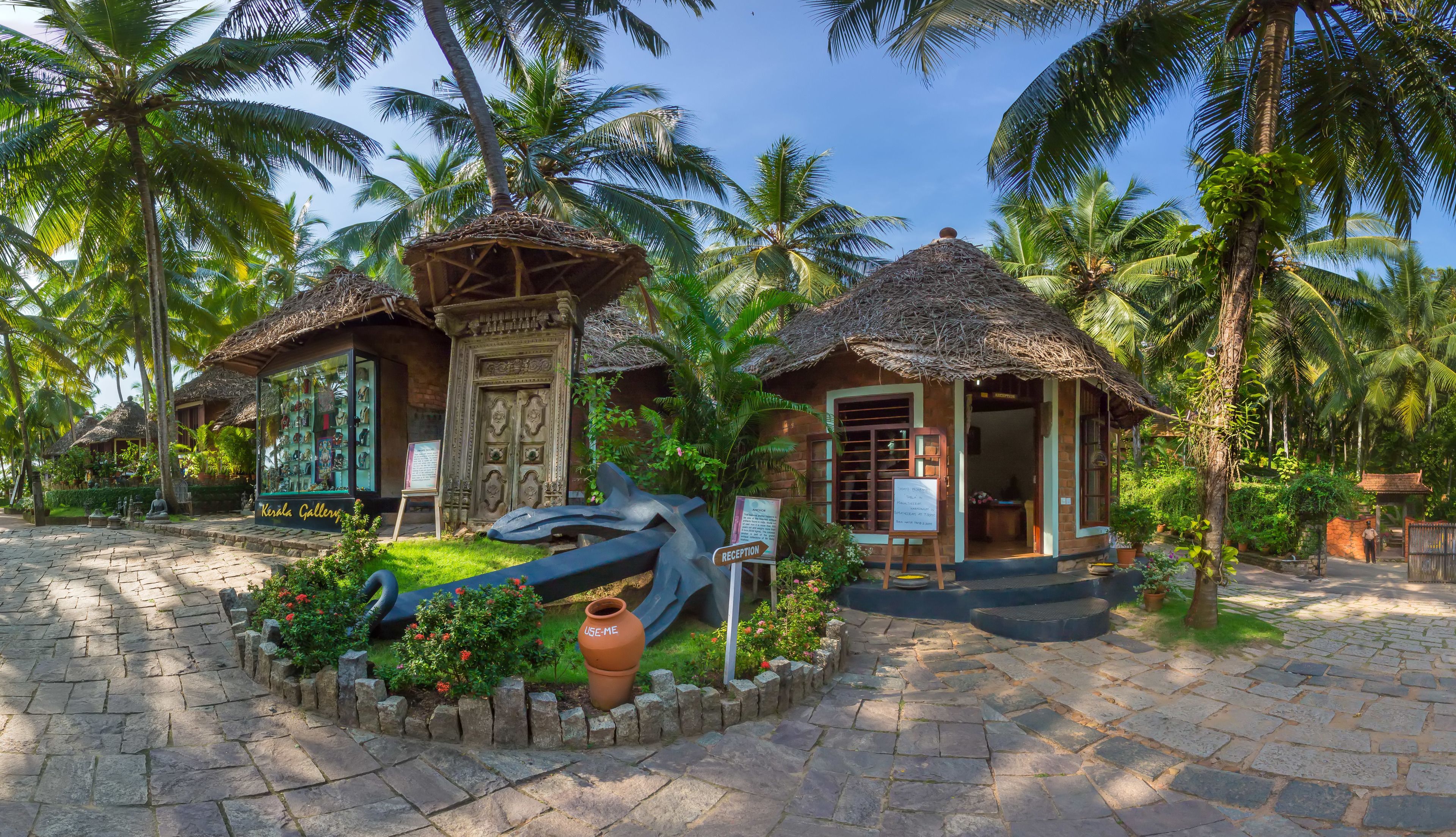 A tropical resort with thatched-roof structures, a reception area, and a garden with potted plants and a large urn.