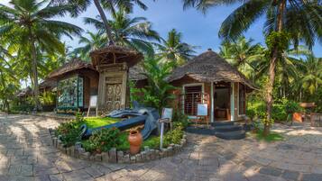 A tropical resort with thatched-roof structures, a reception area, and a garden with potted plants and a large urn.