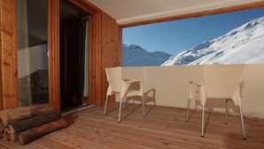 A balcony with wooden flooring, two white chairs, and a glass door leading to a snowy mountain view. - Residence Le Chalet du Mont Vallon (Les Belleville)