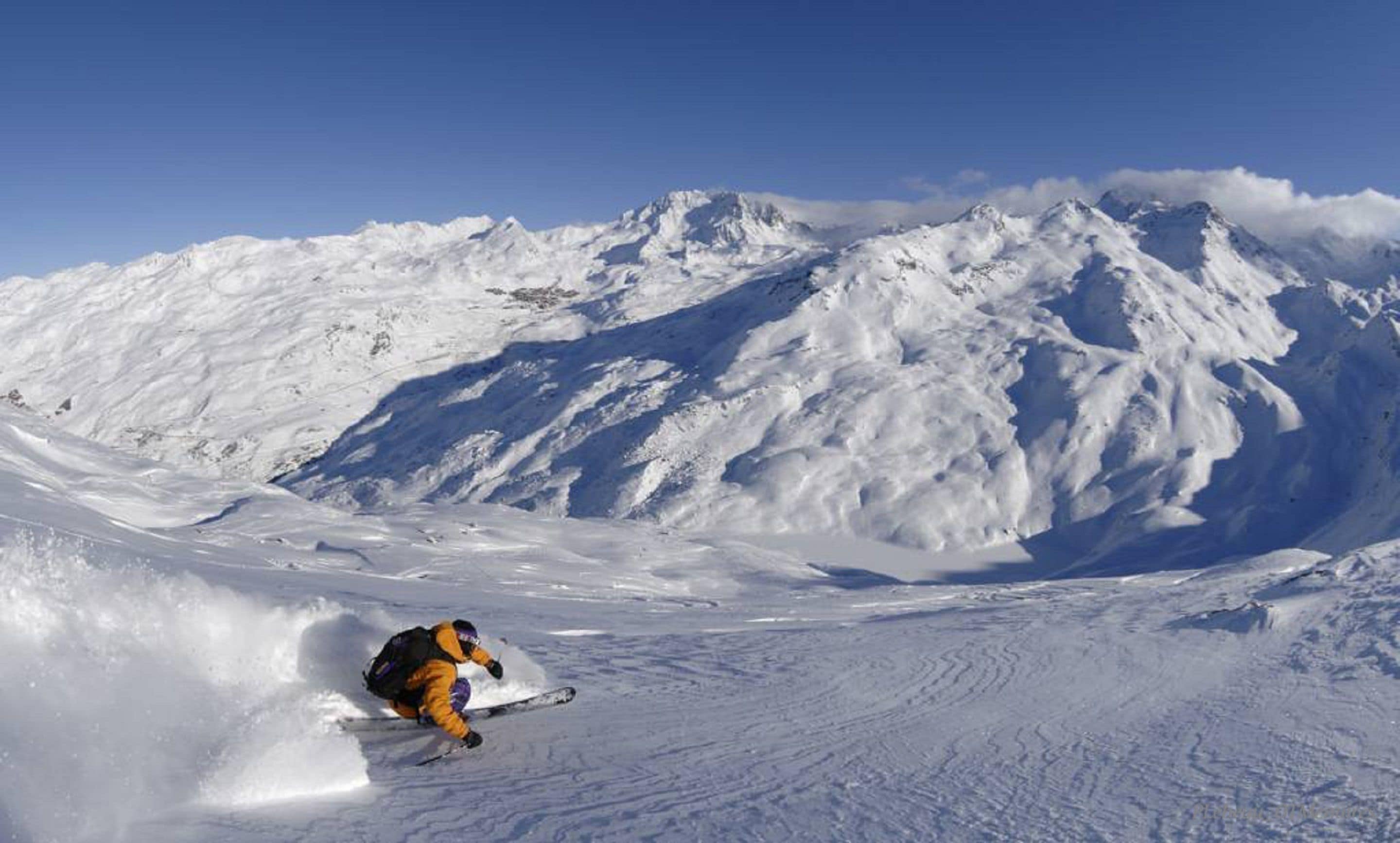 Iemand skiënd op een besneeuwde berghelling, met een heldere lucht.