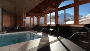 An indoor swimming pool with wooden beams and large windows overlooking a snowy mountain landscape. - Residence Le Chalet du Mont Vallon (Les Belleville)