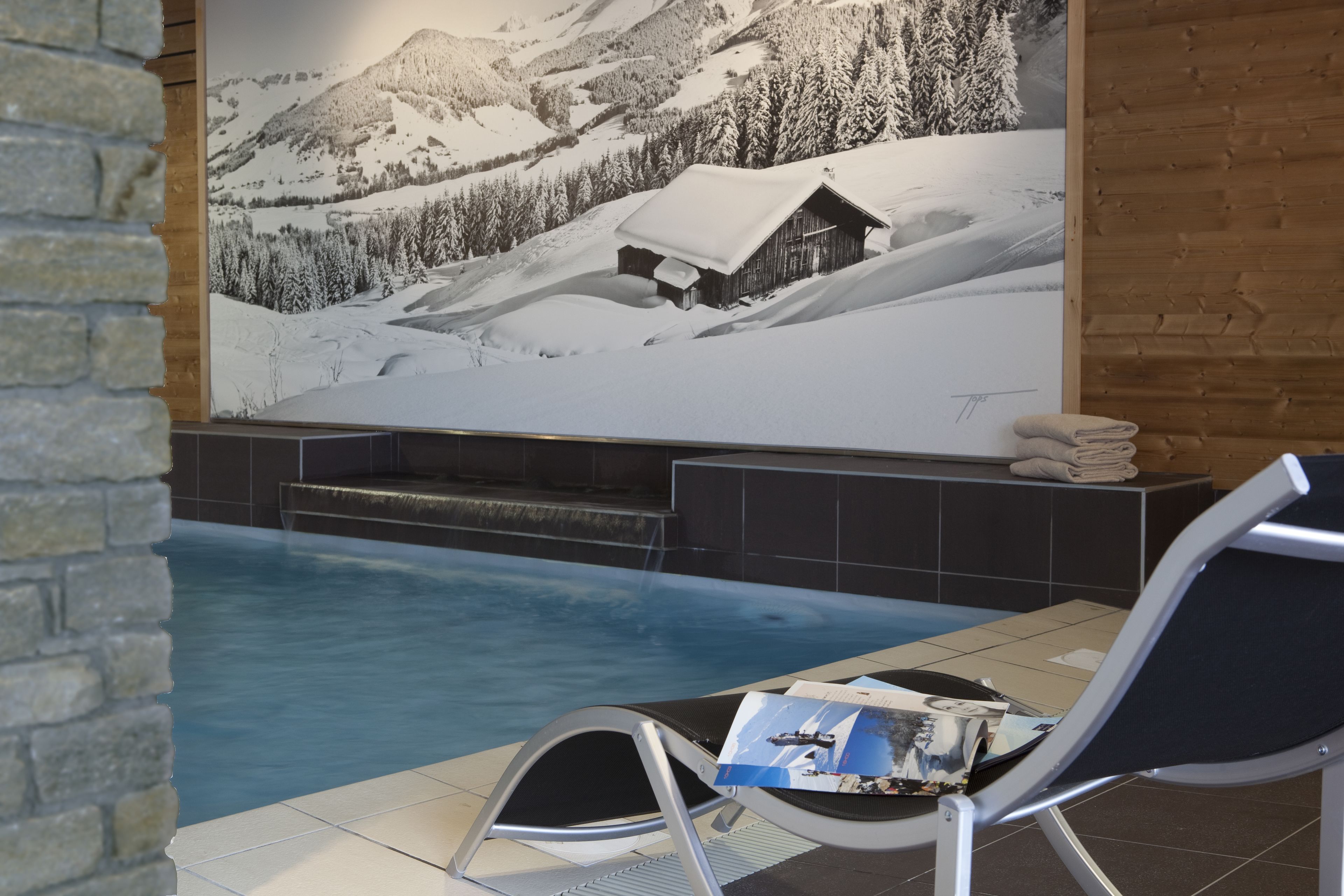 A pool area with a lounge chair, a magazine, and a large wall mural of a snowy mountain scene.