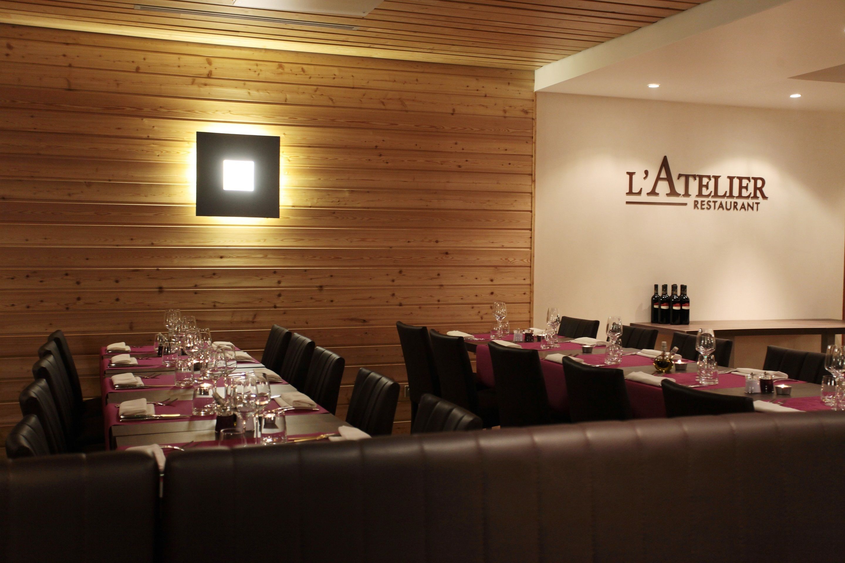 A restaurant interior with wooden panel walls, neatly arranged tables with red tablecloths, and black leather chairs.