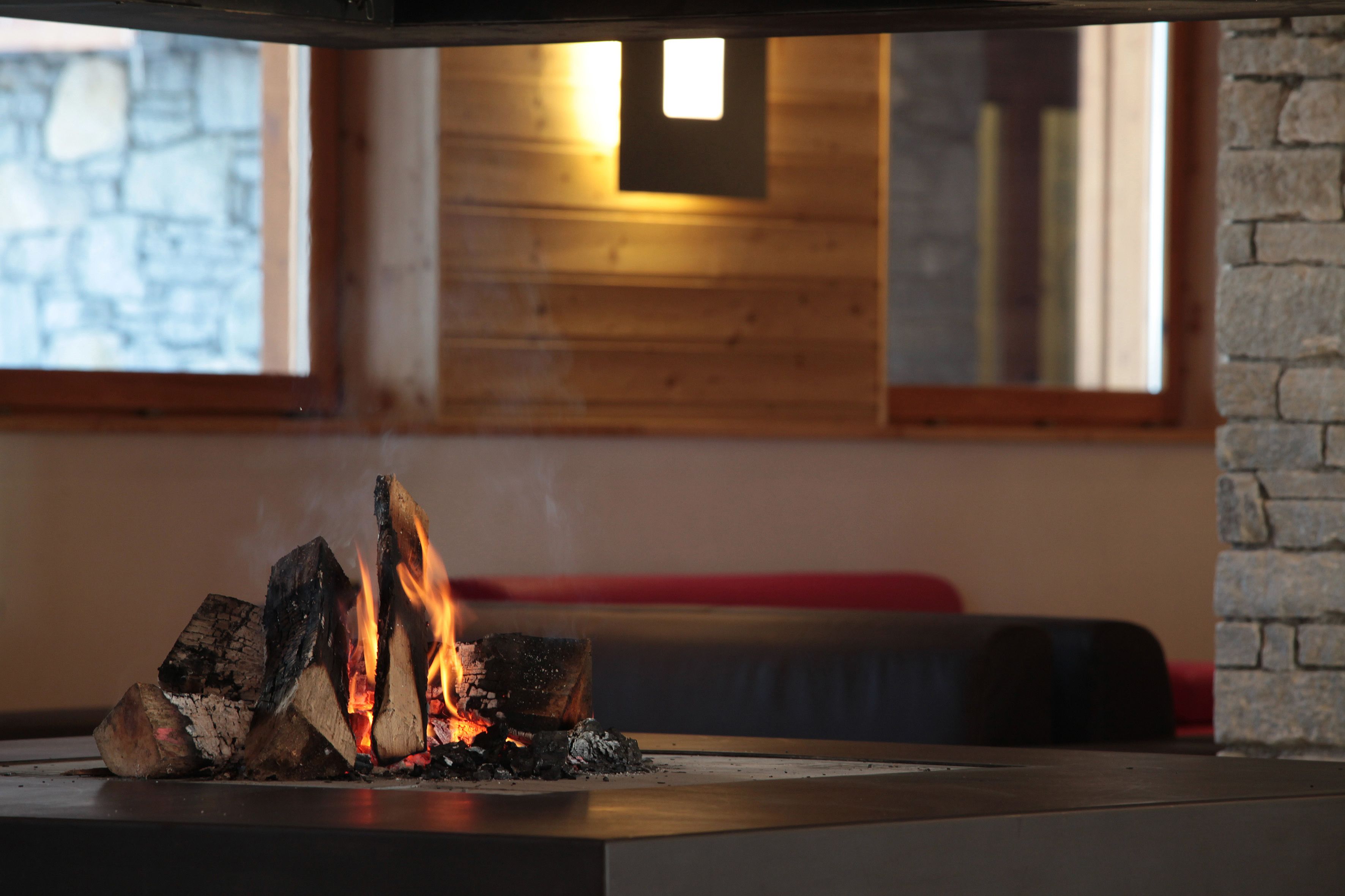 A fireplace with burning logs, a stone wall, and a wooden ceiling in the background.