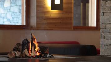 A fireplace with burning logs, a stone wall, and a wooden ceiling in the background.