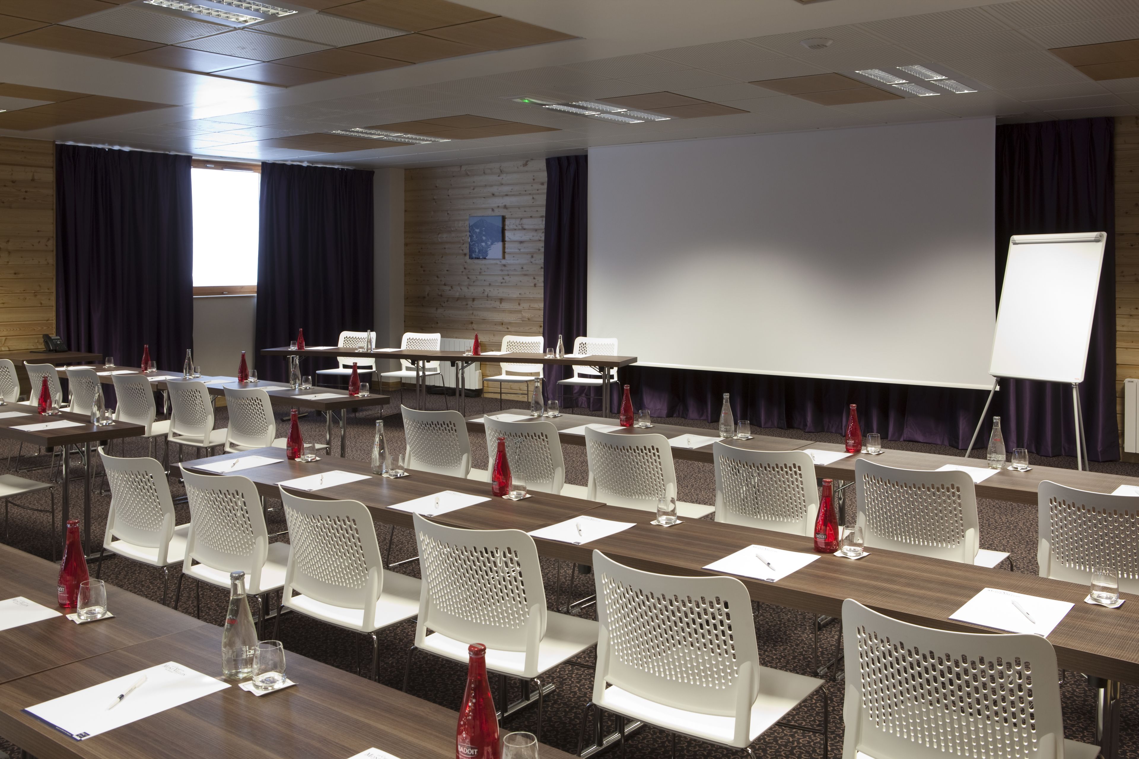 A conference room with multiple tables, white chairs, and a whiteboard.