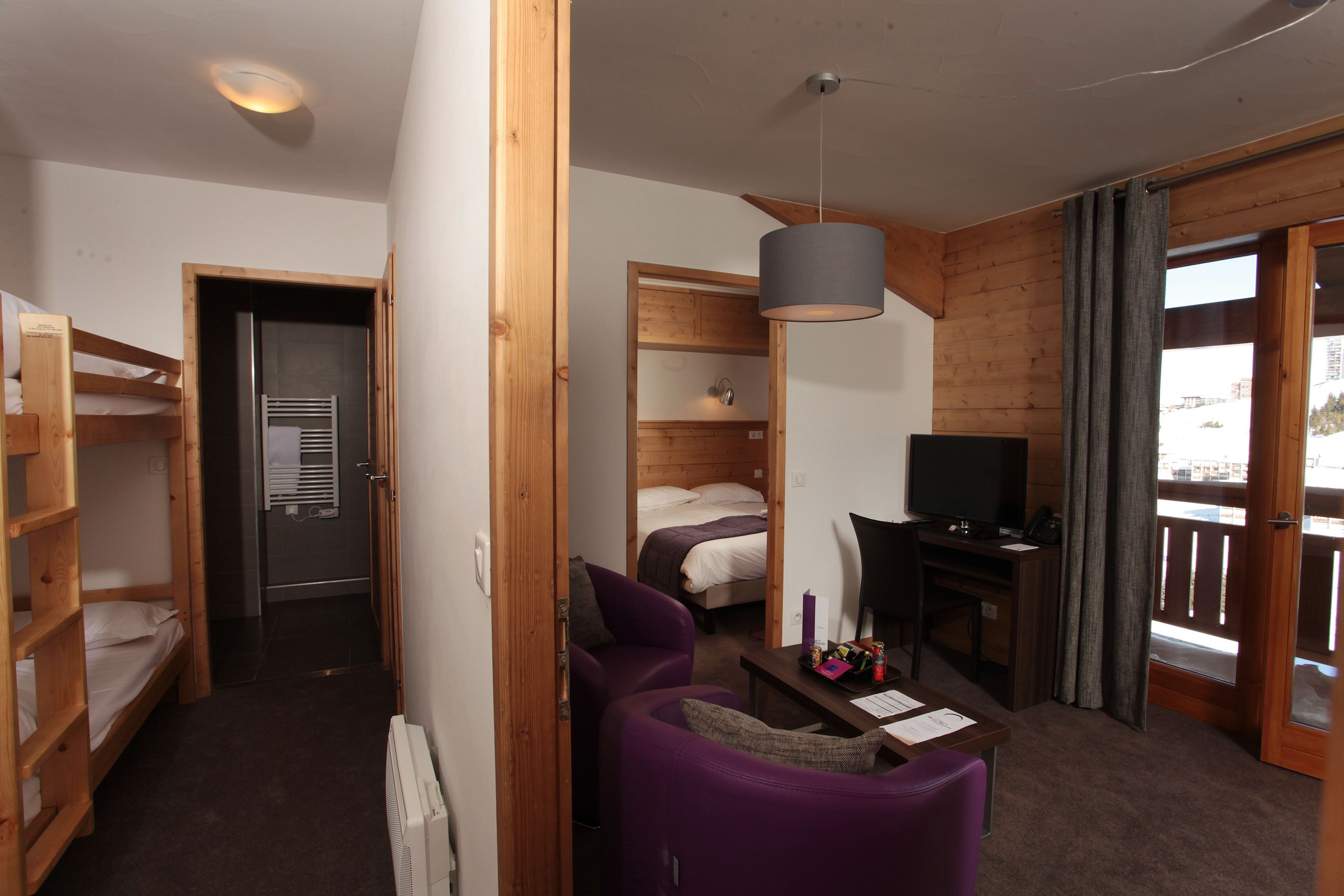 Ein kleines Zimmer mit Etagenbett, Schreibtisch inklusive Computer, einem violetten Sessel und einem Fernseher.