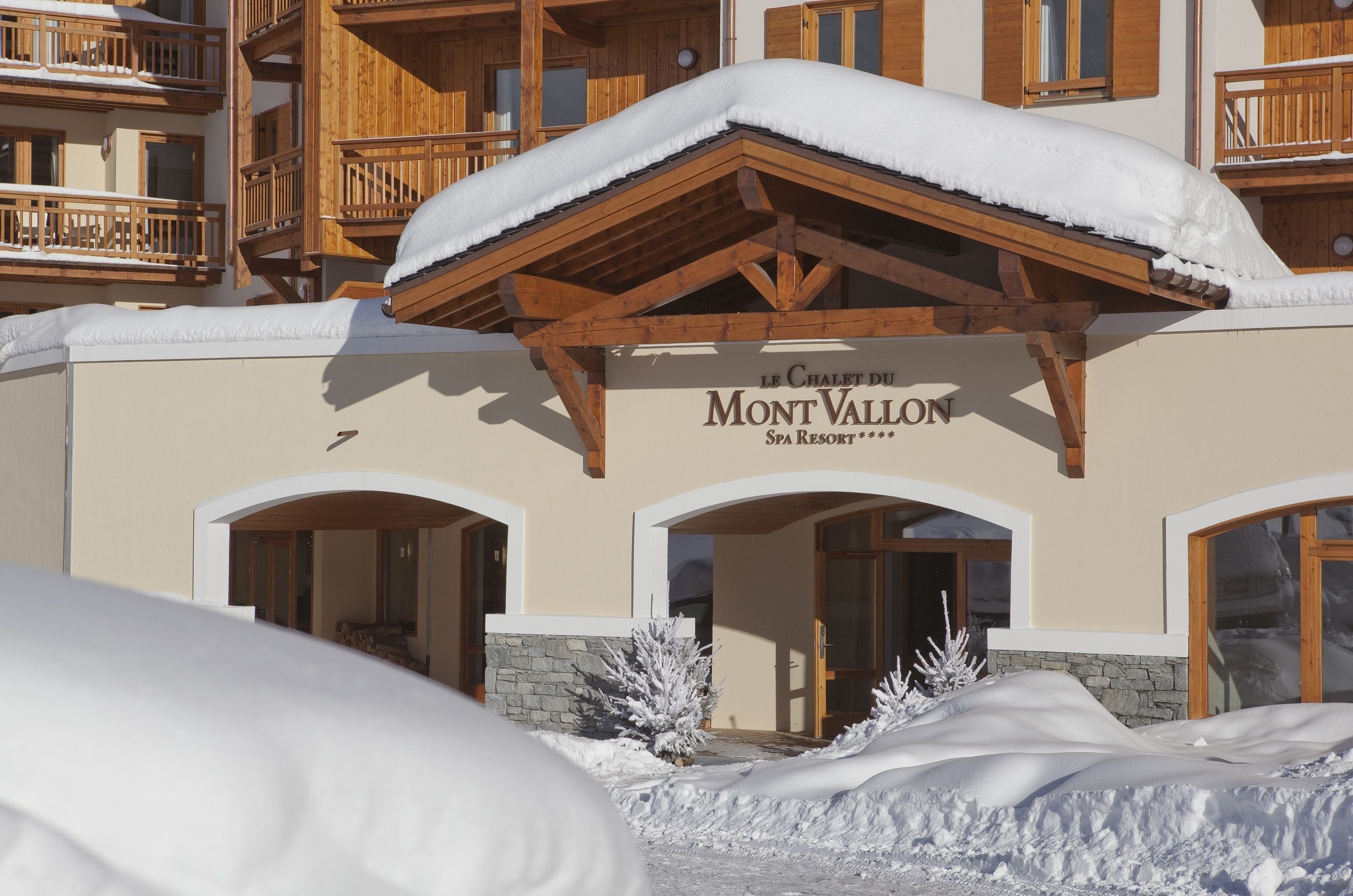 Un hotel con facciata in legno, balconi imbiancati dalla neve e un cartello che riporta la scritta "Le Chalet du Mont Vallon Spa Resort".