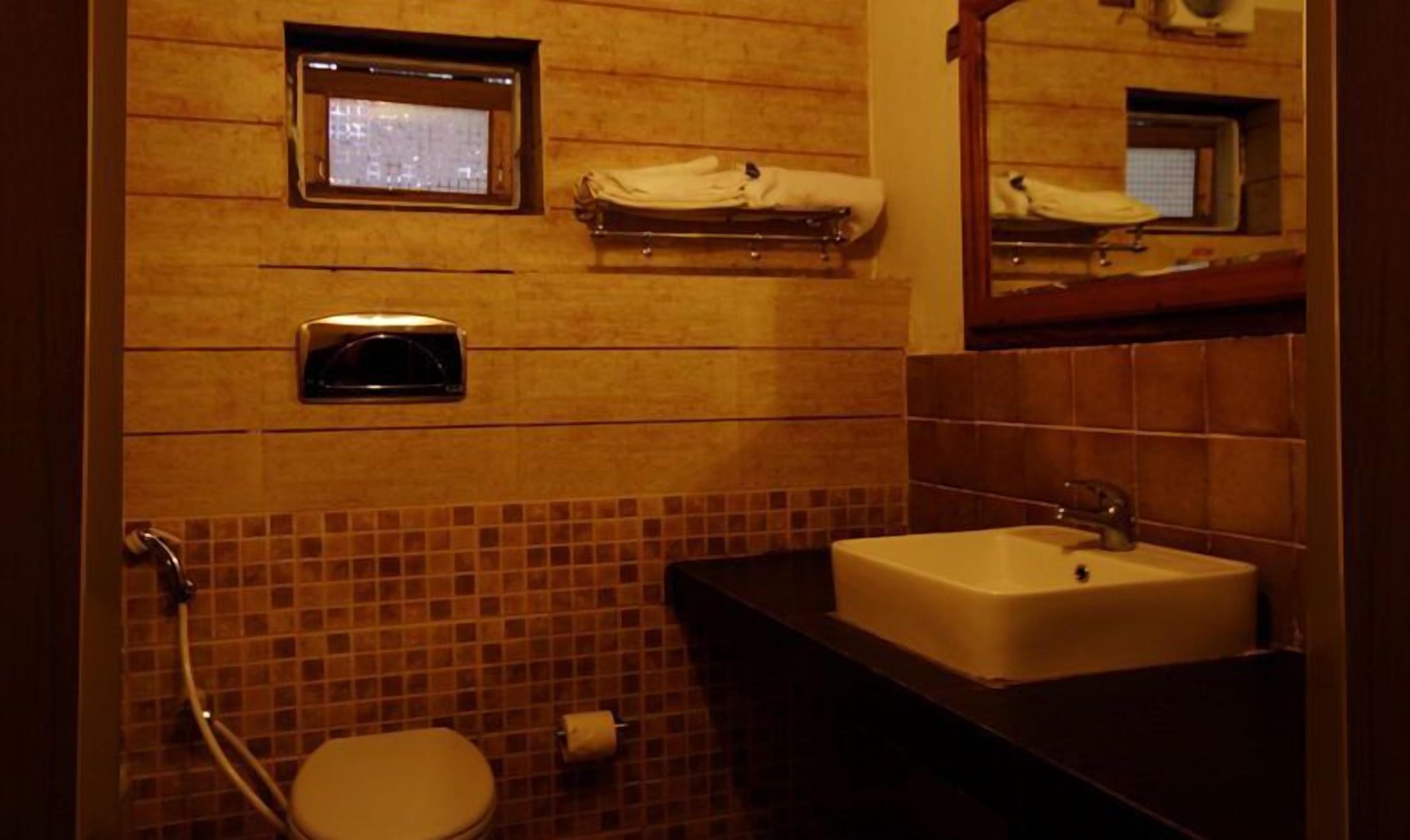 A bathroom with a tiled wall, a sink, a toilet, and a small window.