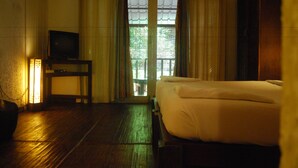 Une chambre avec un lit, un téléviseur posé sur une petite table et une vue sur la verdure à l’extérieur, visible par la porte.