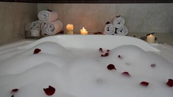 Un baño de spa con pétalos de rosa, velas y toallas enrolladas.