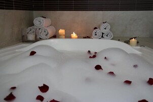Un baño de spa con pétalos de rosa, velas y toallas enrolladas.