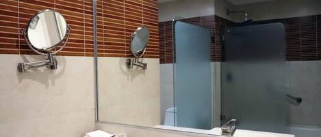 Une salle de bain avec un lavabo blanc, deux miroirs fixés au mur et une cabine de douche en verre.