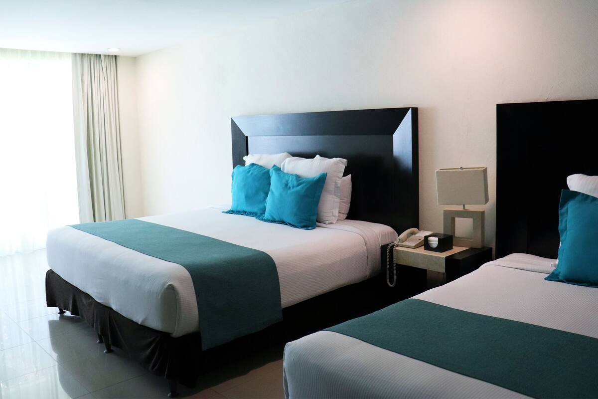 Ein Hotelzimmer mit zwei Betten, einem Nachttisch mit Telefon und einem Fenster mit Vorhängen.