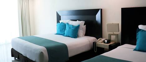 Una habitación de hotel con dos camas, una mesita de noche con un teléfono y una ventana con cortinas.